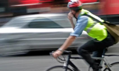 A man wearing a helmet and Hi Vis jacket is riding a bike. A silver car is passing on the opposite side of the road. 