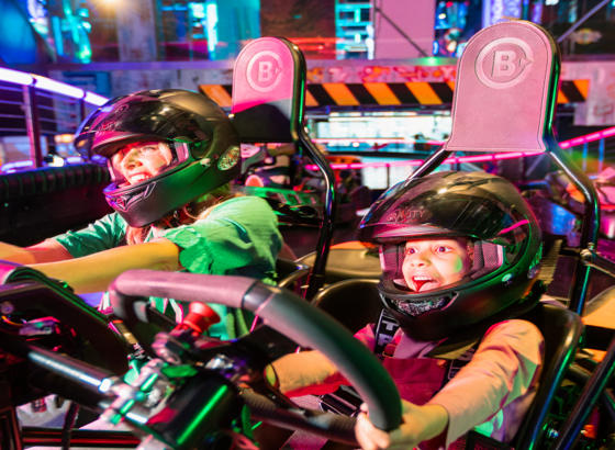 Two people wearing helmets driving a go kart.