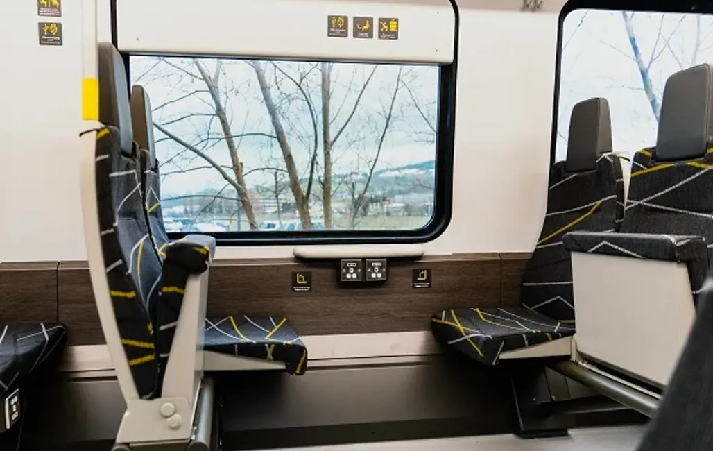 Seats on a 777 train. There are branches outside the window. 