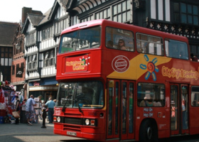 A red tour bus driving around a busy Chester street.