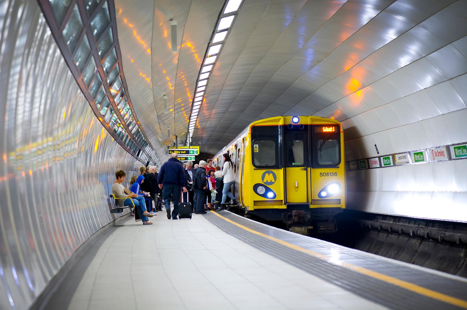 Passengers leaving a Merseyrail train at a busy underground station platform.