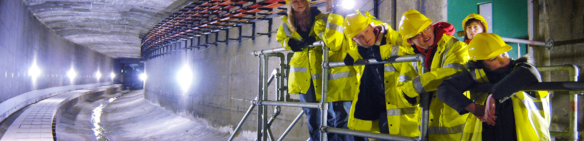 People in brightly lit vests and hats inside a large underground tunnel.