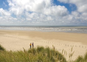Sandy beach, with sandunes and a cloudy blue sky.