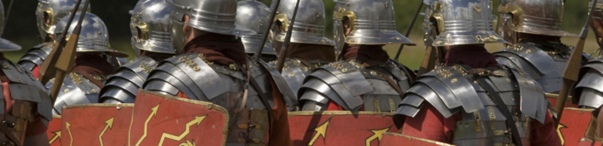 A group of people dressed as romans with helmets and red and yellow shields.