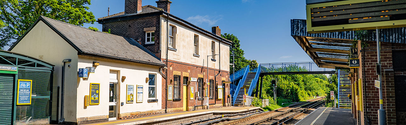 The platform at Hightown station. A blue pedestrian footbridge and the ticket office appears. 