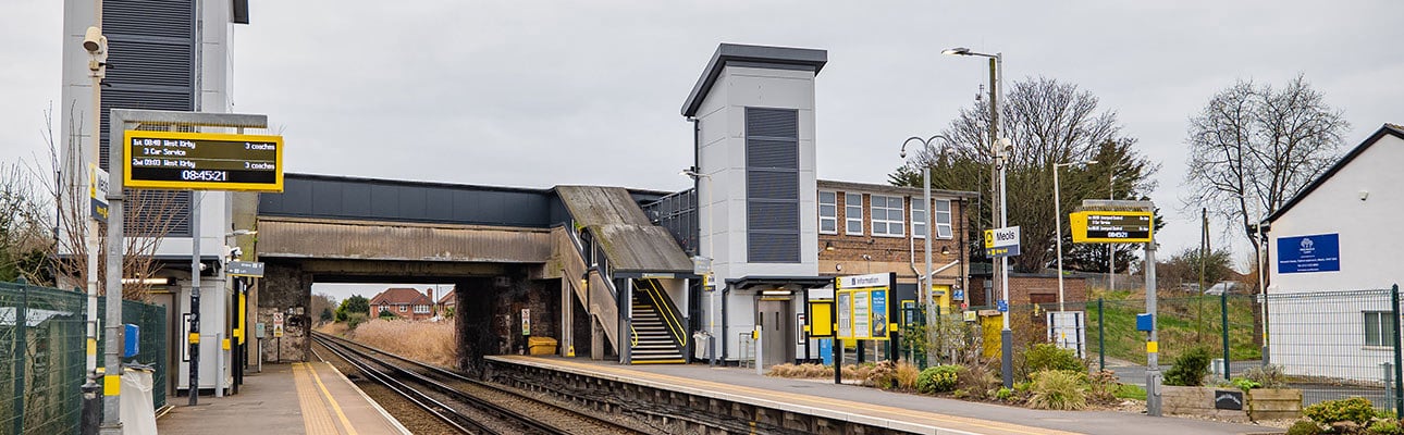 The platform at Meols station. A tall station building and a bridge appear. There is digital information signage on the platform. 