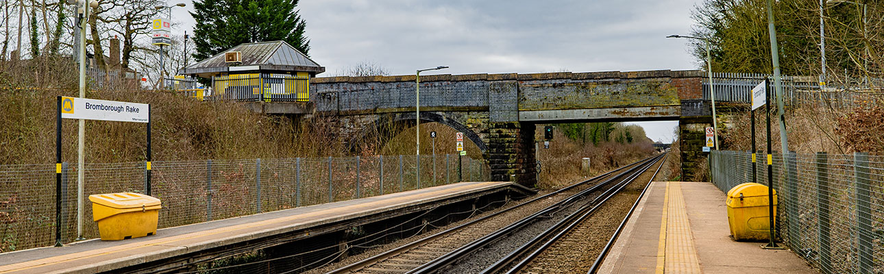 The railway track at Bromborough Rake station. There is signage and an overarching bridge above the track. A ticket office also appears.