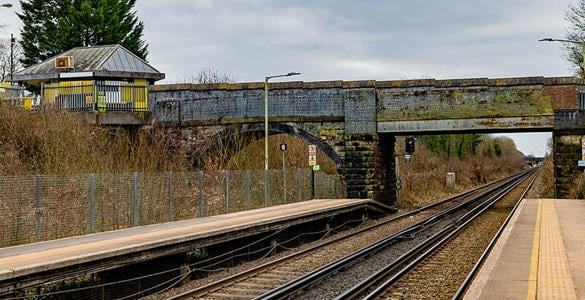 The railway track at Bromborough Rake station. There is signage and an overarching bridge above the track. A ticket office also appears.