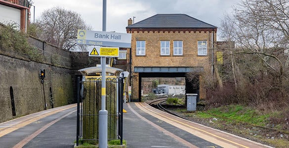 Bank Hall station platform. A tall wall and ticket office are overlooking the railway track. 