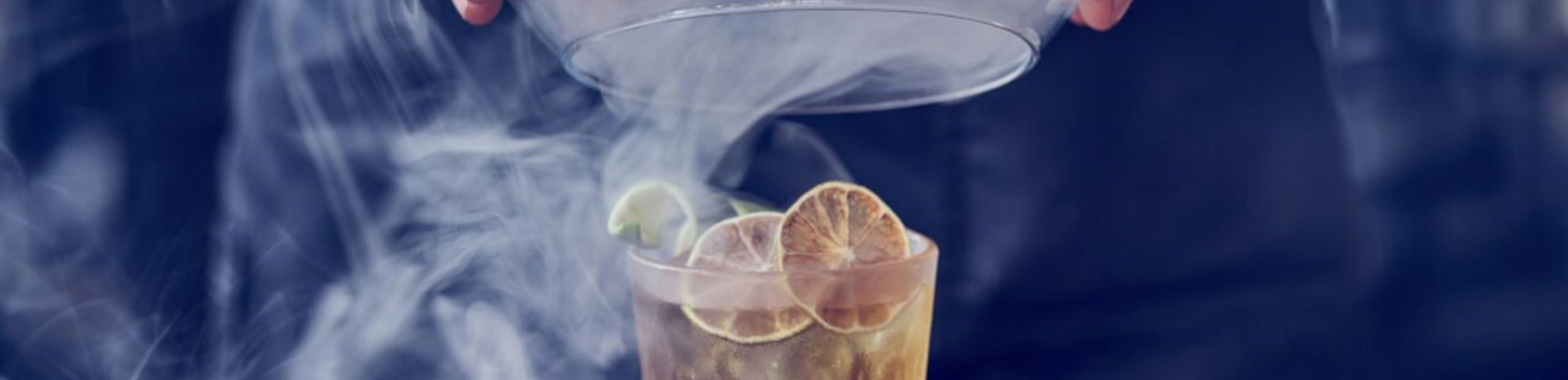 A bartender pouring a cocktail, with smoke coming out of it. 