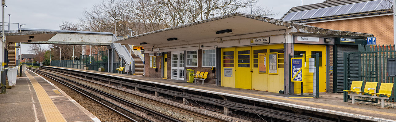 The platform at Manor Road station. There is a pedestrian footbridge, outdoor seating and a station building.