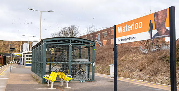 The platform at Waterloo station. A sign with the station name appears. There is seating and a bike shed. 