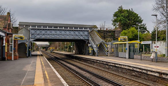 The platform at Wallasey Grove Road station. A pedestrian footbridge appears above the railway track. Sheltered seating areas also appear on the platform. 