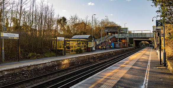 The platform at Fazakerley station. Sheltered seating, station signage appear. The station ticket office and a bridge are in the distance. 