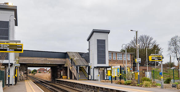 The platform at Meols station. A tall station building and a bridge appear. There is digital information signage on the platform. 