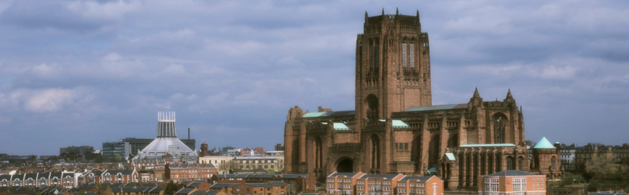 Two Liverpool Cathedrals are shown in the distance. There is a cloudy blue sky above. 