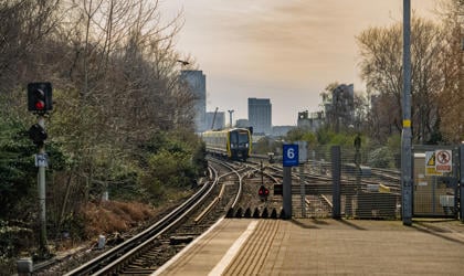 A 777 train approaching a platform. The city landscape appears in the background.  