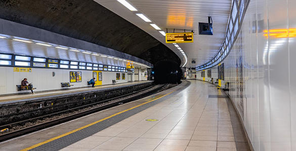 The underground station platform at Hamilton Square. Digital signage boards and lights appear. Passengers are seated waiting for a train. 