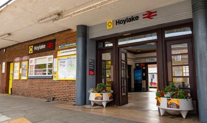 The entrance of Hoylake station. Large planters with flowers are shown each side of open wooden doors.  