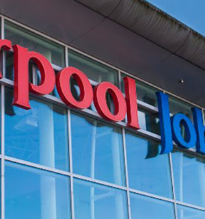 Signage of Liverpool John Lennon Airport's logo on a glass building. A blue sky appears above. 