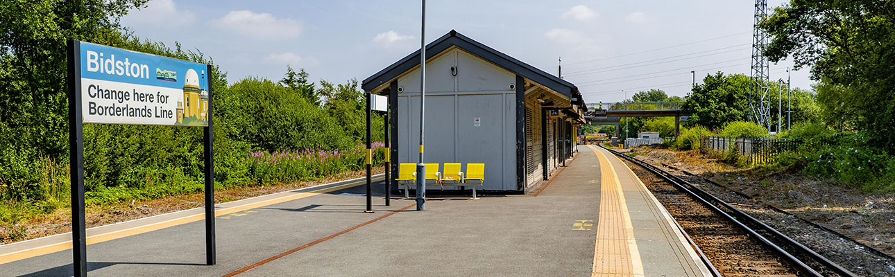 An outdoor seating area and station signage on the platform at Bidston station. 