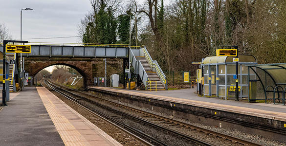 An empty platform at Capenhurst Station. There is a bridge above the train track and sheltered seating for passengers. 