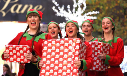 A happy group of Christmas elves holding presents walking through Liverpool ONE
