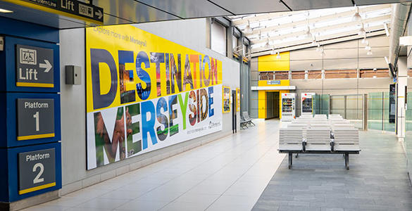 A seating area at Liverpool Central Station. There is colourful signage promoting Merseyrail's 'Destination Merseyside' website.
