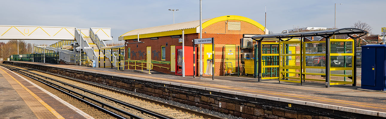 The ticket office at Aintree station. The platform, railway track and a pedestrian footbridge appear. 