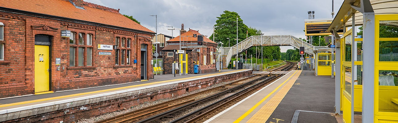The platform at Hall Road station. A pedestrian footbridge and station ticket office appear. 