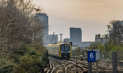 A 777 train approaching a station. The city skyline appears in the background. 