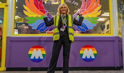 A member of Merseyrail staff stood in front of a colourful mural at a Merseyrail station. 