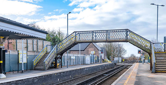 The platform at Maghull station. There are stairs and a pedestrian footbridge above the platform and railway tracks.