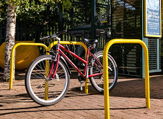 A bike tied to a bike stand at a station. Information posters and Amazon lockers appear in the background. 