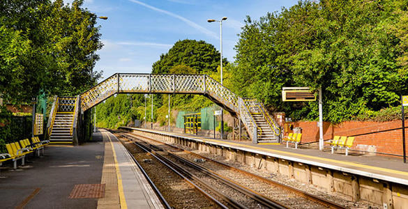 The platform at Rice Lane station. There is seating and signage on the platform. A pedestrian footbridge appears in the distance. 