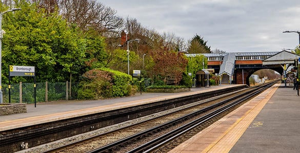 An empty platform at Bromborough station surrounded by bushes and trees. There are lampposts and a stairway to the ticket office. 