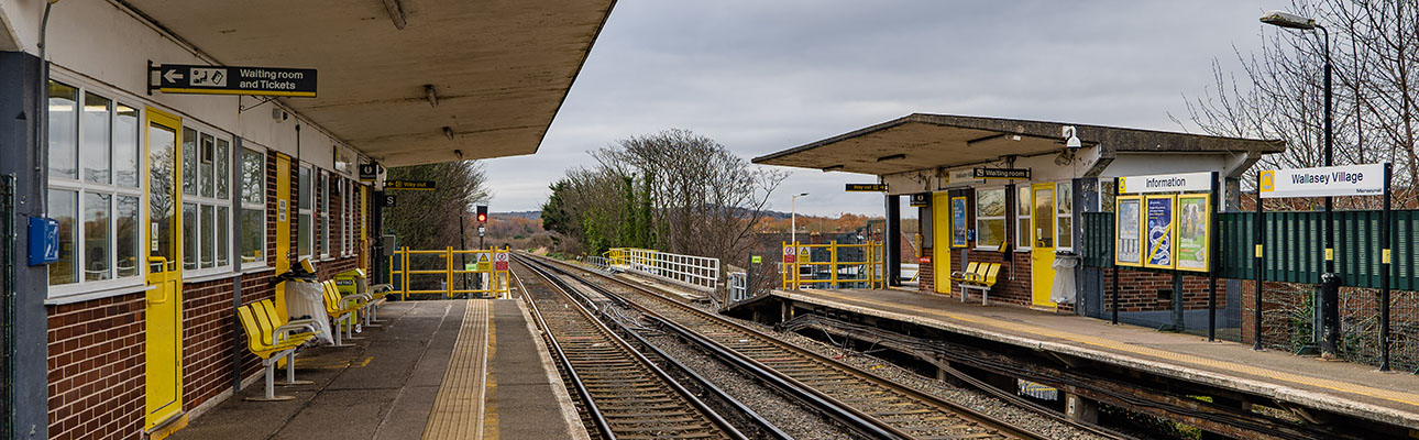 The platform and railway tracks at Wallasey Village station. There is sheltered seating and information signage on the platform. 