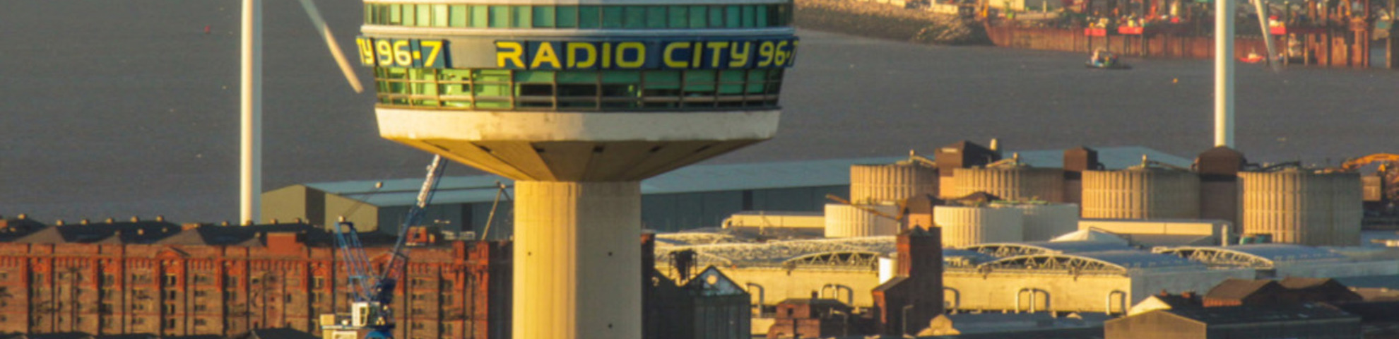 The top of the radio city tower at sunset. Buildings are in the background.