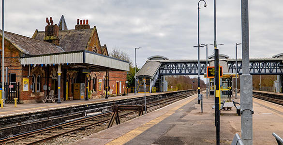 The platform at Hooton station. A pedestrian footbridge and sheltered seating appear. 