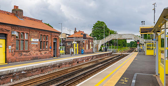 The platform at Hall Road station. A pedestrian footbridge and station ticket office appear. 