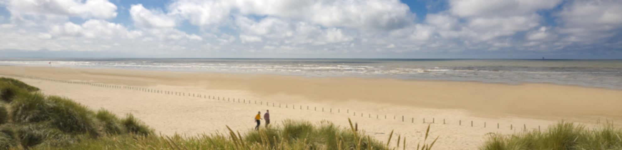 Sandy beach, with sandunes and a cloudy blue sky.